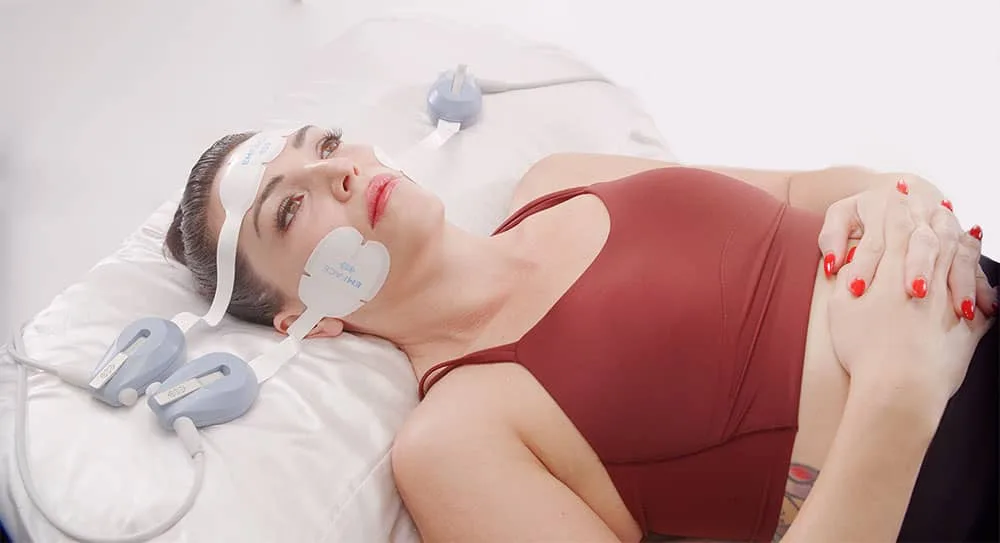 Woman lying down with facial applicators in place at our Harley Street clinic, EMface facial toning London